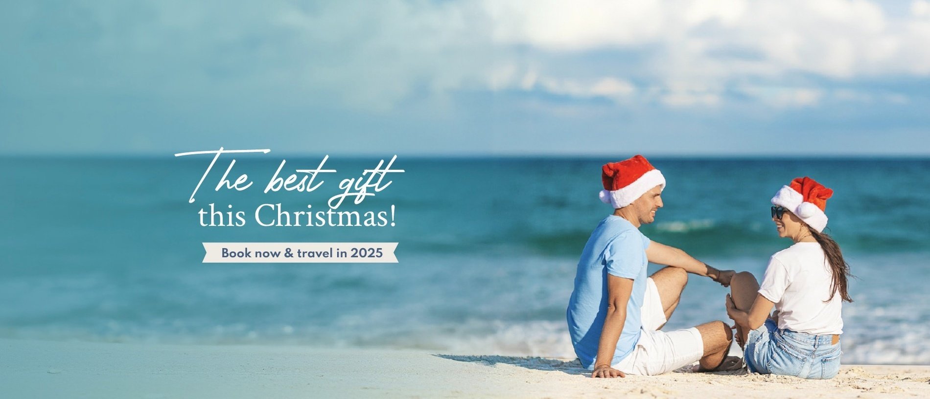 a man and woman wearing santa hats sit on the beach