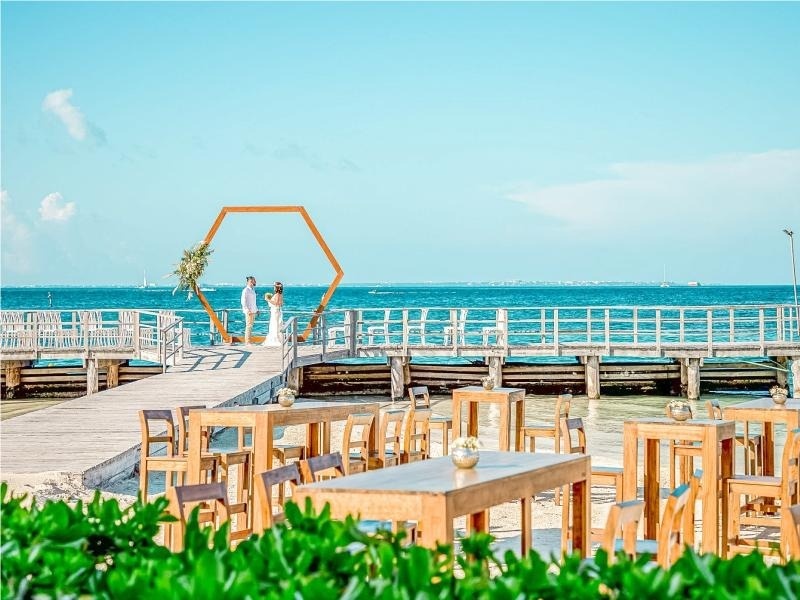 a bride and groom are standing on a pier overlooking the ocean .