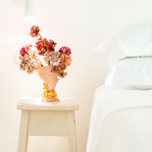 a vase of flowers sits on a stool next to a bed