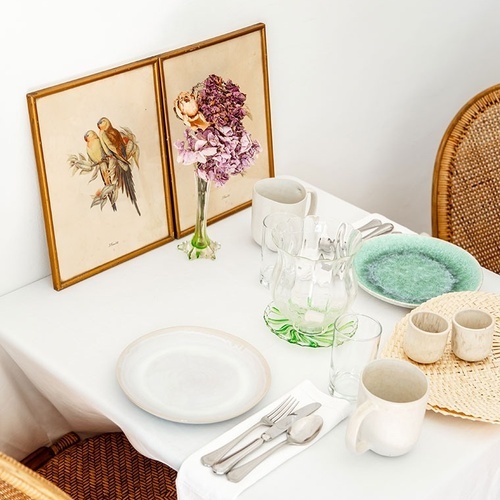 una mesa con platos y tazas y dos cuadros de pájaros