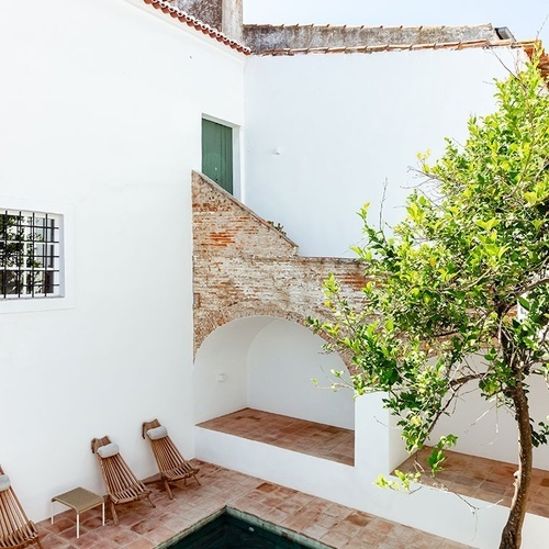 uma piscina com uma árvore ao lado de uma casa branca