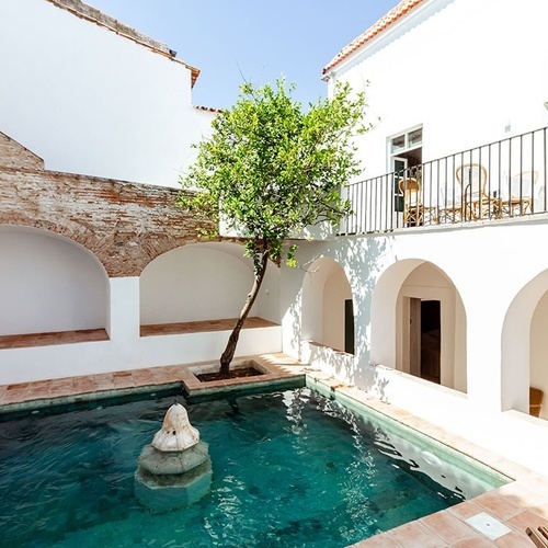 una piscina rodeada de edificios blancos y un árbol