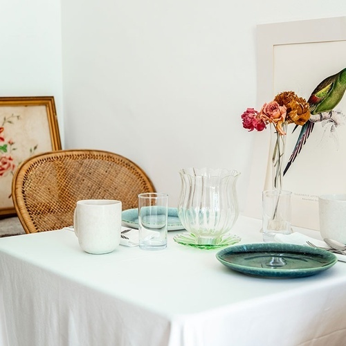 una mesa con platos y vasos y una pintura de un pájaro en la pared