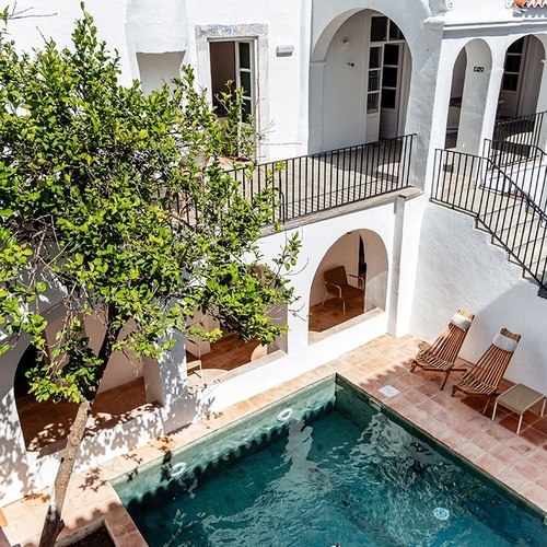 una piscina rodeada de edificios blancos y un árbol