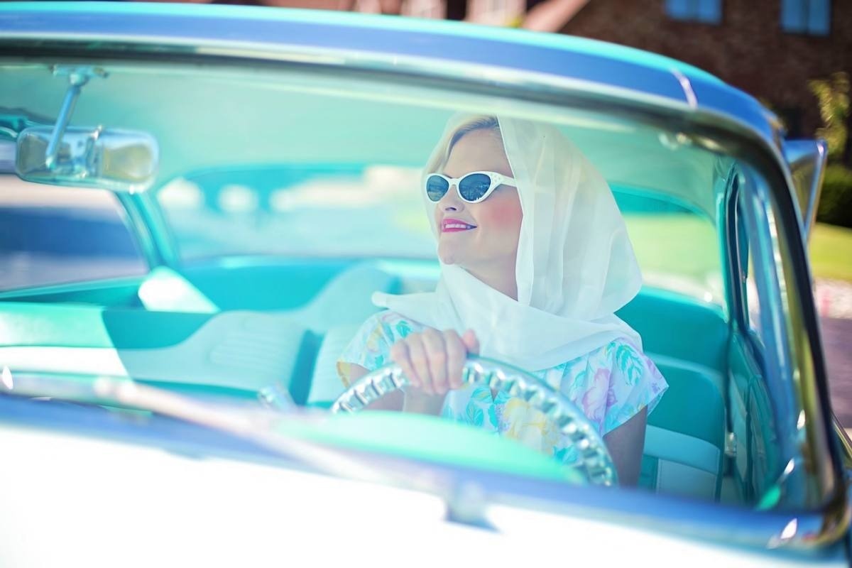 a woman wearing sunglasses and a scarf is driving a car