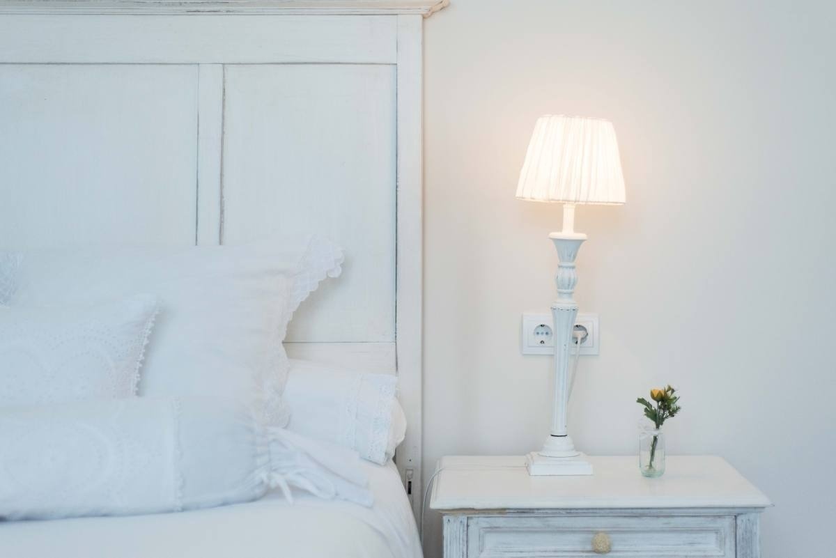 a white lamp sits on a nightstand next to a bed