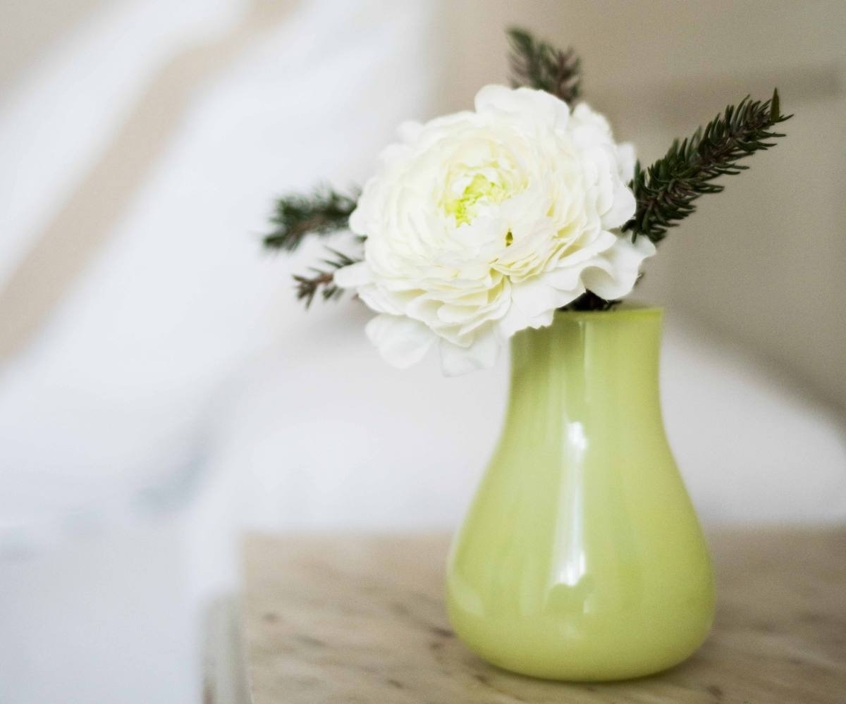 a green vase with a white flower in it