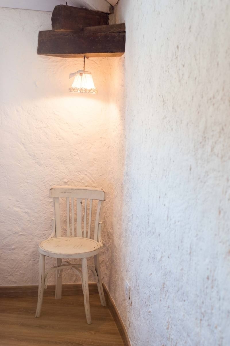 a white chair sits in a corner of a room under a lamp