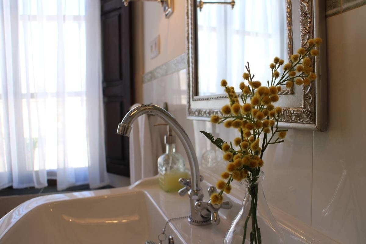 un jarrón de flores amarillas está sobre un lavabo junto a un espejo