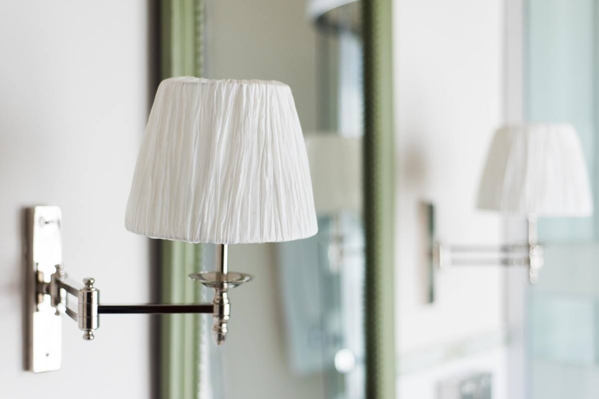 una lámpara de pared con un pantalla blanca y un espejo en el fondo
