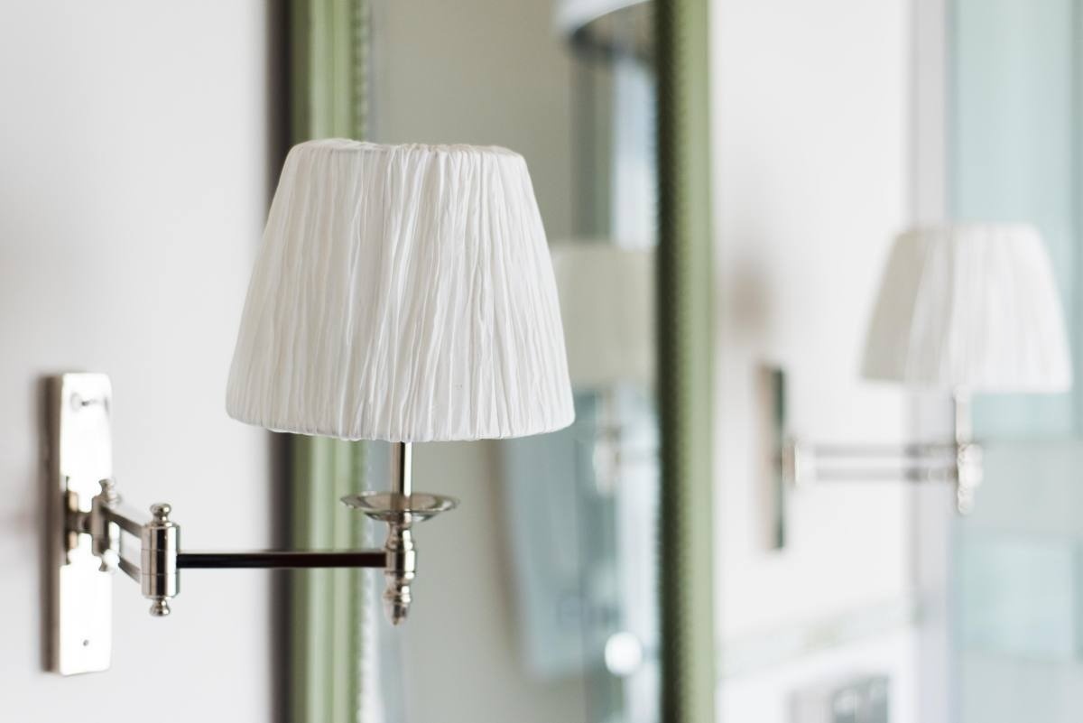 a lamp with a white pleated shade is hanging on a wall next to a mirror