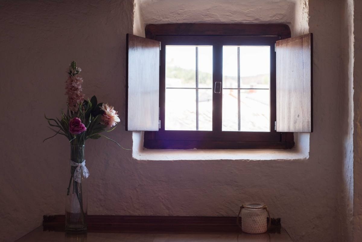 un jarrón de flores se sienta junto a una ventana con persianas de madera