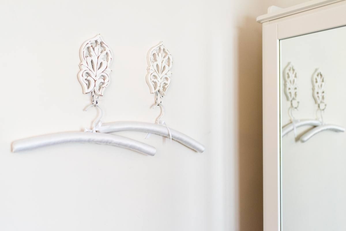 two white clothes hangers hanging on a white wall next to a mirror