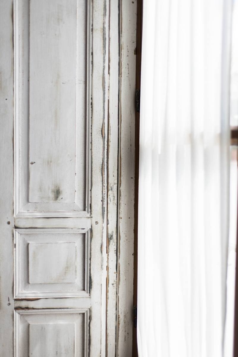 una puerta de madera blanca junto a una ventana con cortinas blancas