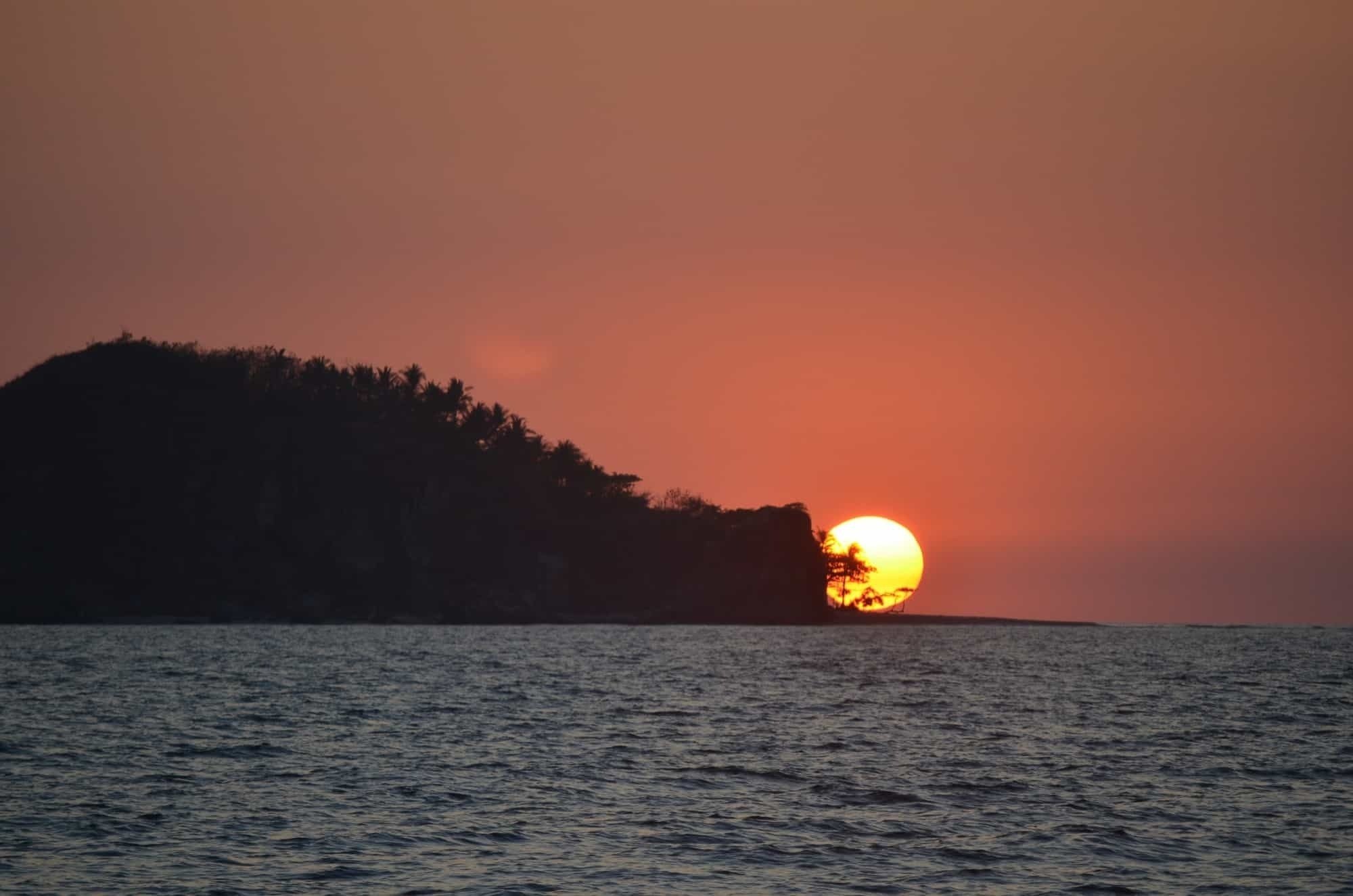 the sun is setting over a small island in the middle of the ocean