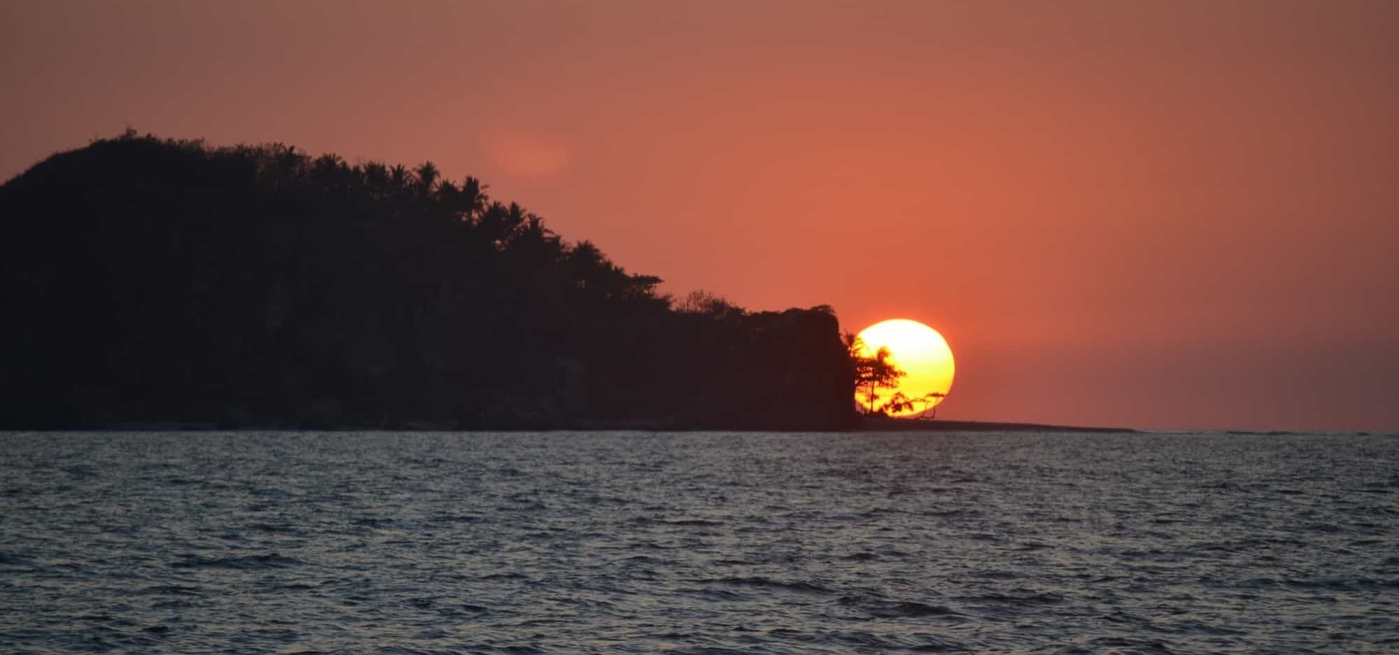 le soleil se couche derrière une petite île dans l' océan