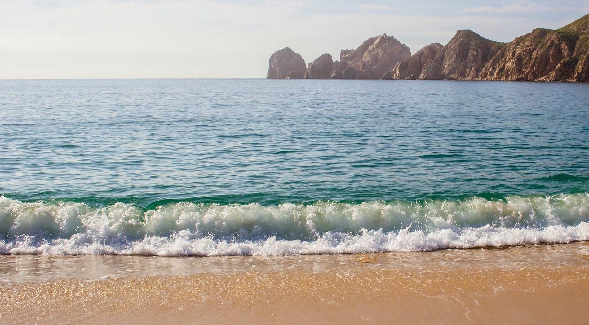 waves crashing on a sandy beach with mountains in the background
