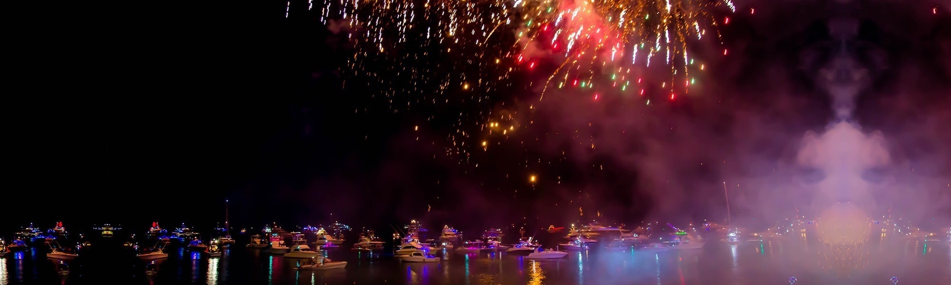 un grupo de barcos están flotando en el agua durante un espectáculo de fuegos artificiales .
