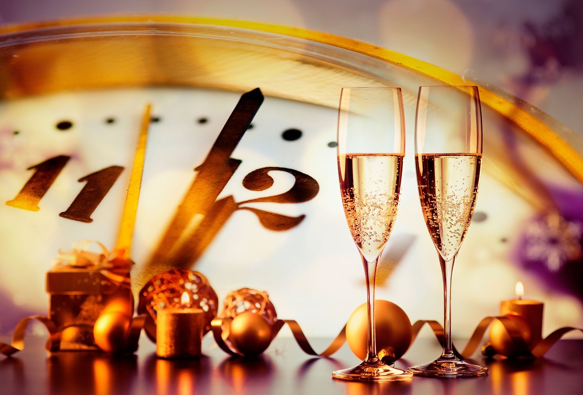 two glasses of champagne are sitting in front of a clock with the hands on the numbers 11 and 12