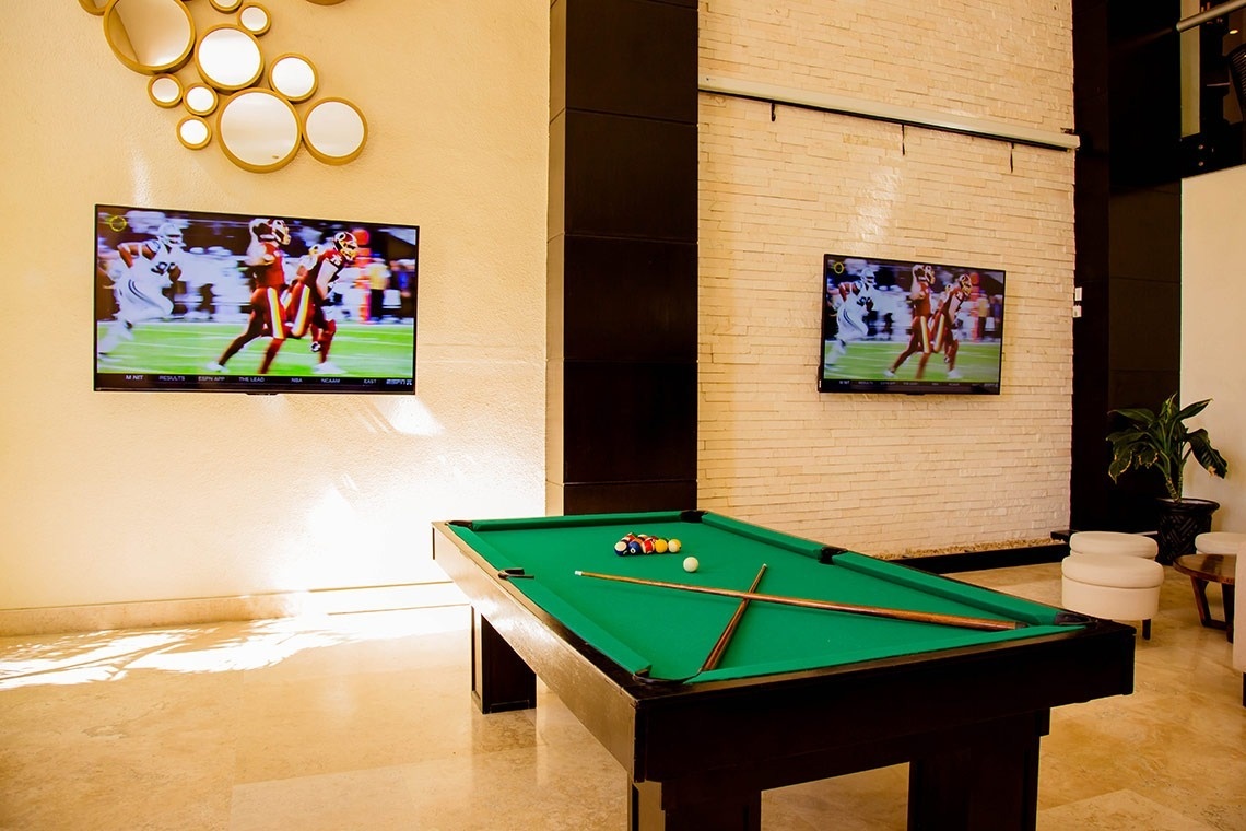 a pool table with two televisions on the wall behind it