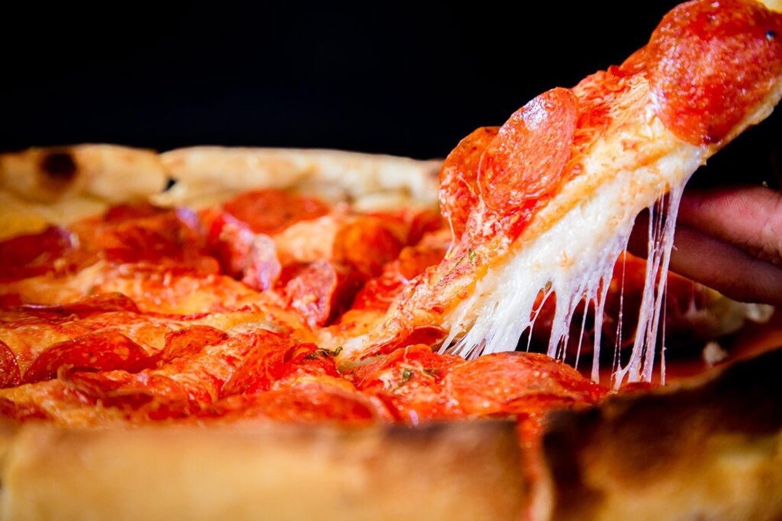 a person is taking a slice of pepperoni pizza