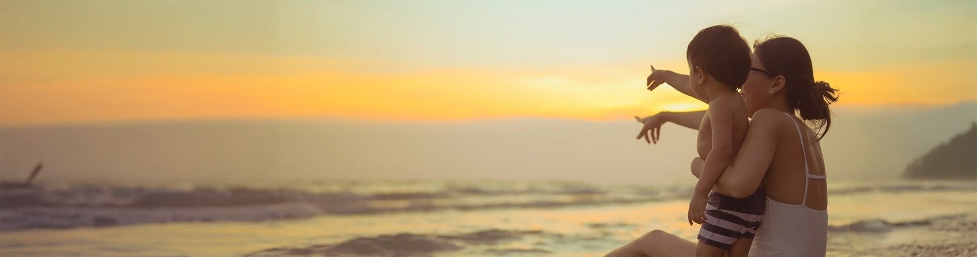 Eine Frau sitzt mit einem Kind am Strand und zeigt auf den Sonnenuntergang
