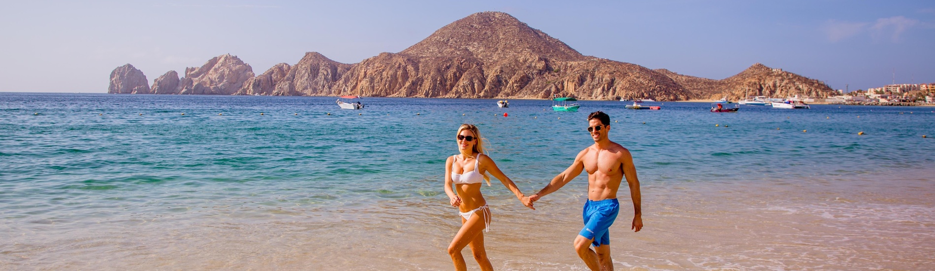 Couple walking in shallow waters at Casa Dorada beach resort with scenic mountains.
