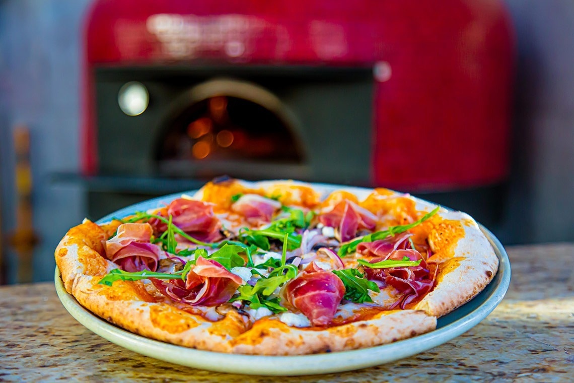 une pizza sur une assiette blanche devant un four rouge