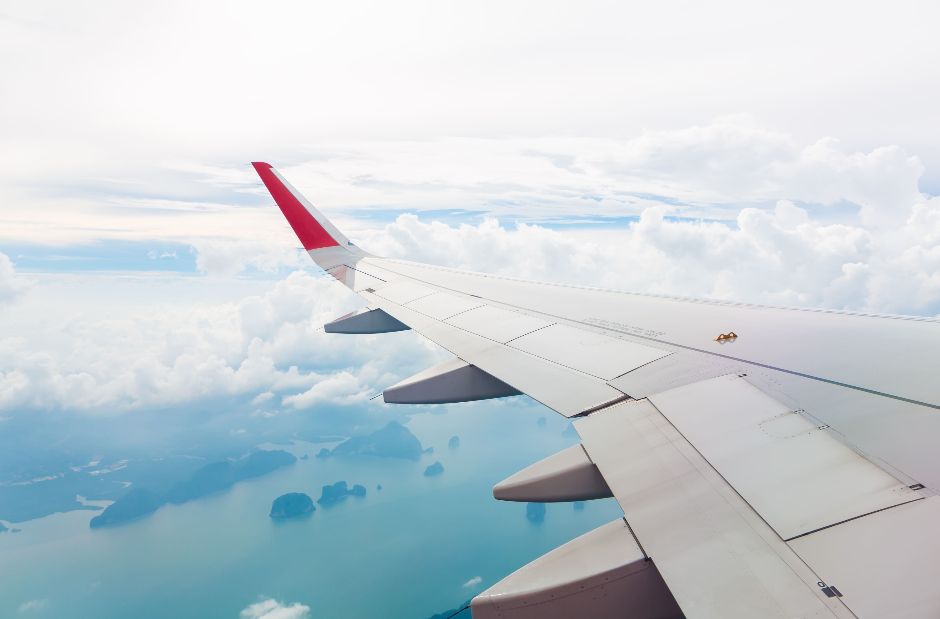 an airplane wing with a red tail is flying over a body of water