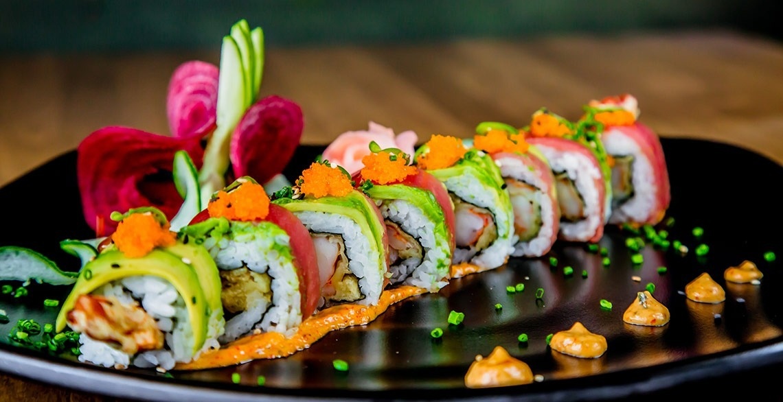 a black plate topped with sushi rolls and sauces