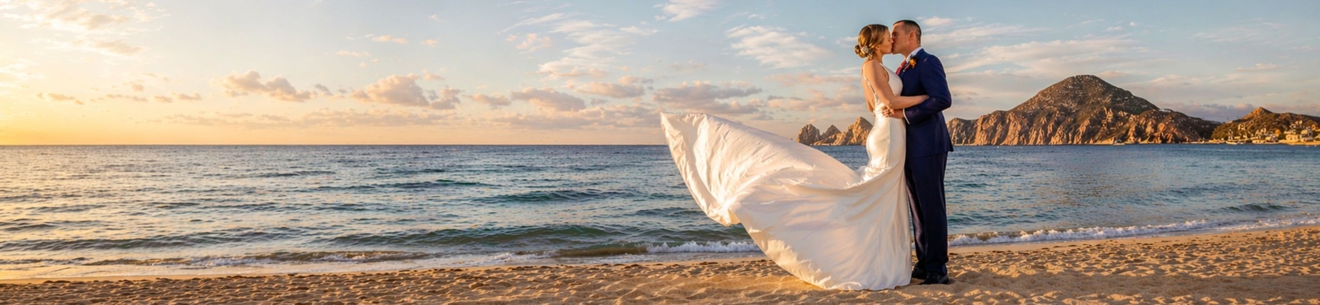 Mariage de destination romantique: couple s'embrassant sur la plage au coucher du soleil, vue mer et montagnes.