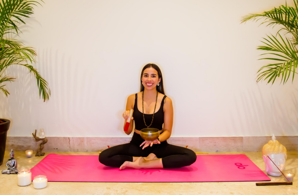 a woman sits on a yoga mat holding a bowl