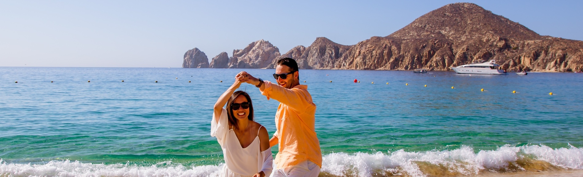 ein Mann und eine Frau tanzen am Strand mit einem Boot im Hintergrund