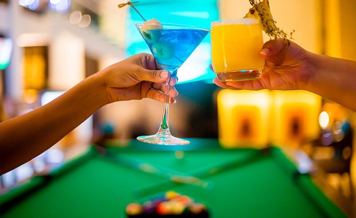 dos personas sostienen cócteles frente a una mesa de billar