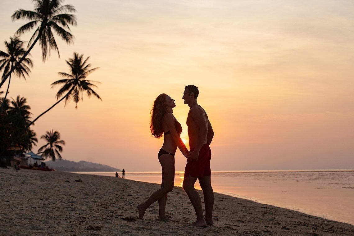 a man and a woman holding hands on a beach at sunset