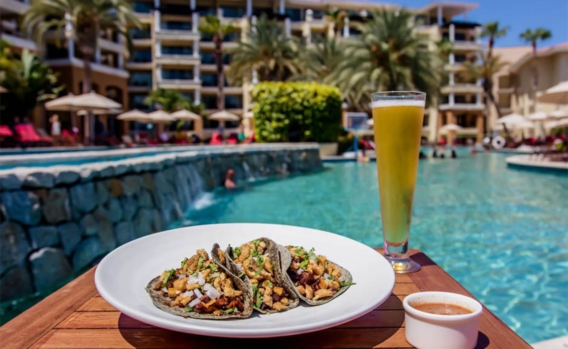 un plato de tacos y un vaso de cerveza junto a una piscina
