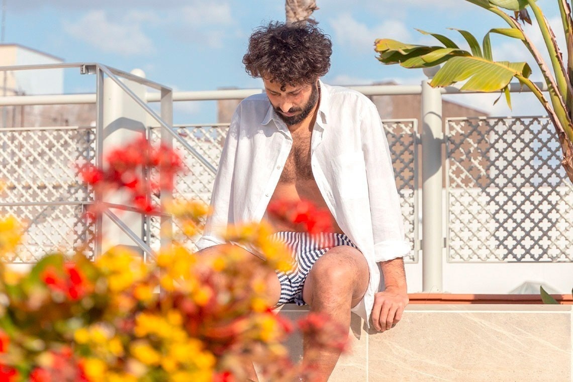 un hombre sin camisa y pantalones cortos se sienta en un balcón