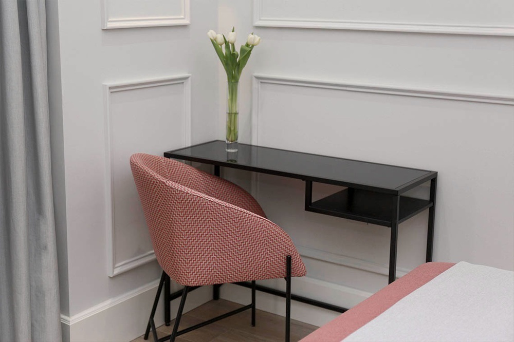 a chair sits next to a desk with a vase of flowers on it