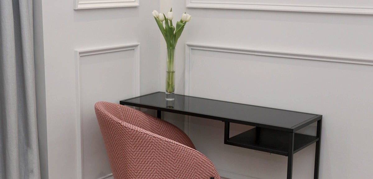a chair sits next to a desk with a vase of flowers on it