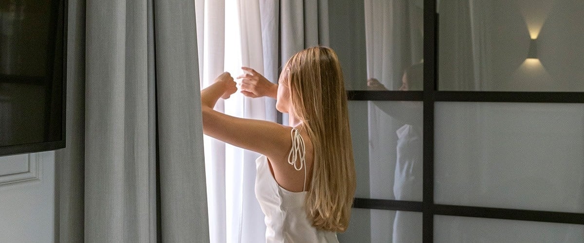 una mujer abriendo las cortinas de una ventana
