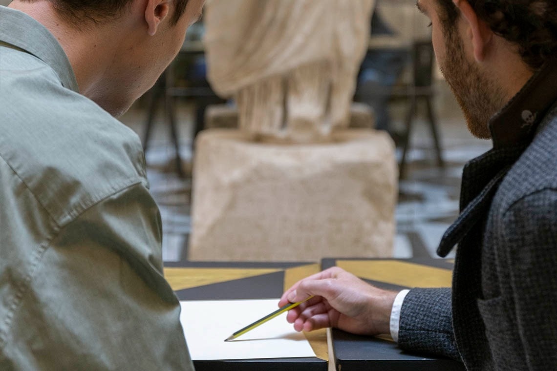 two men looking at a piece of paper with a statue in the background