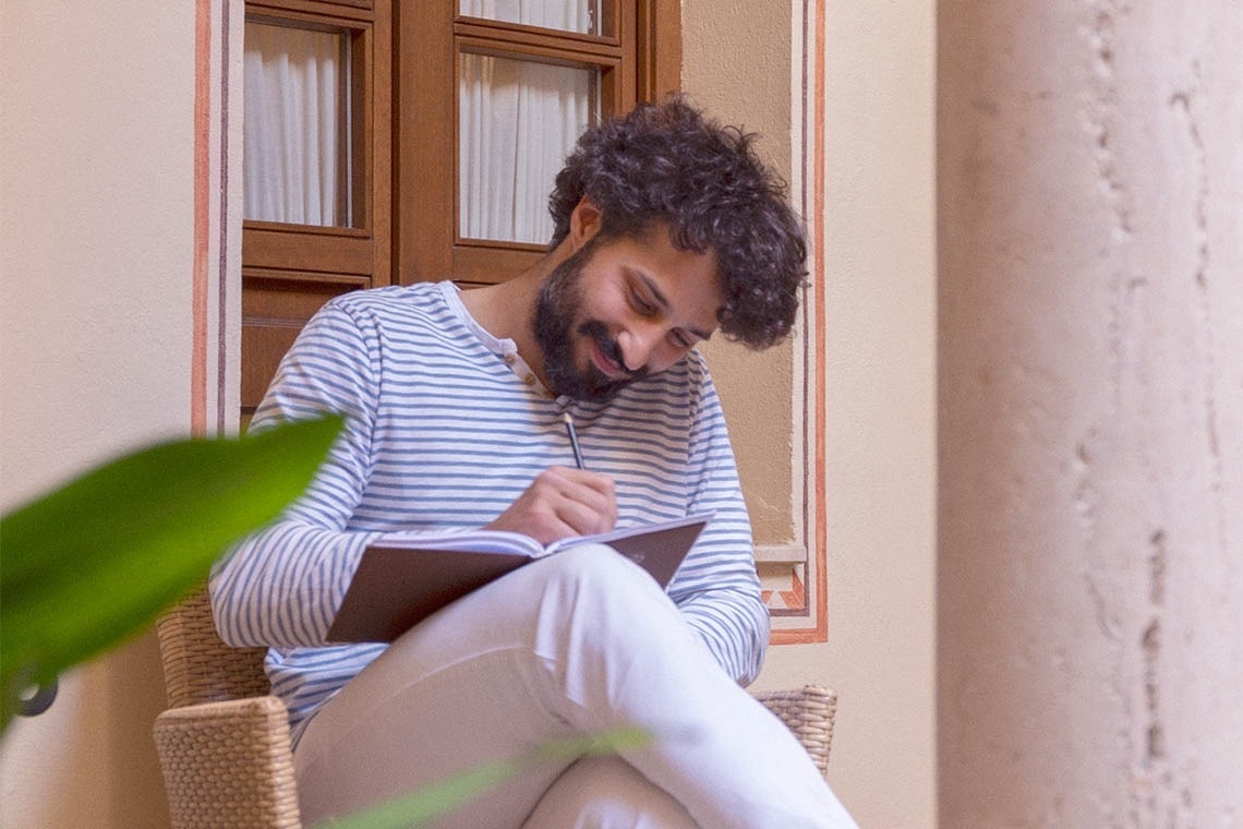 un hombre con barba está sentado en una silla y escribiendo en un cuaderno