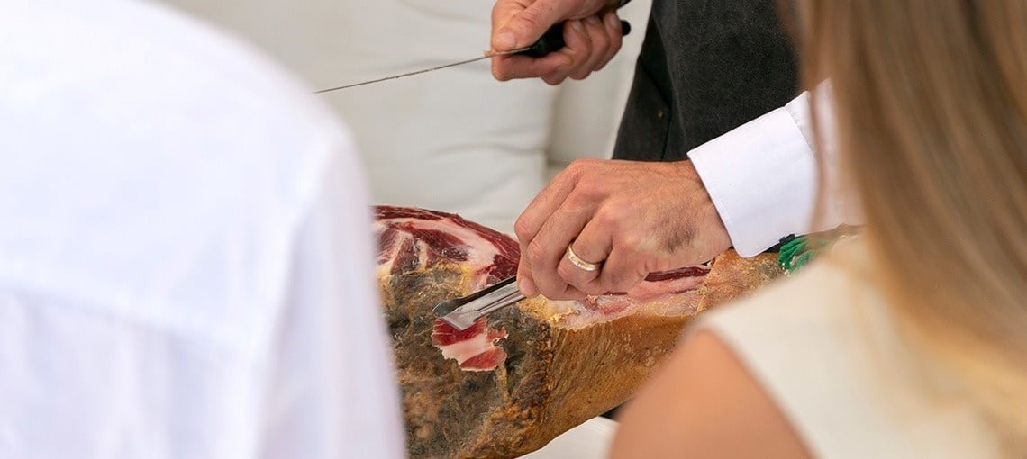 un hombre corta un trozo de jamón con un cuchillo