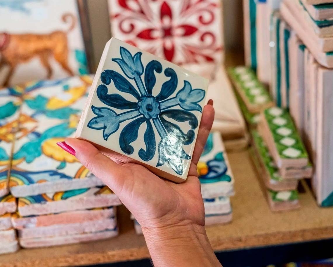 a person holding a tile with a blue flower design