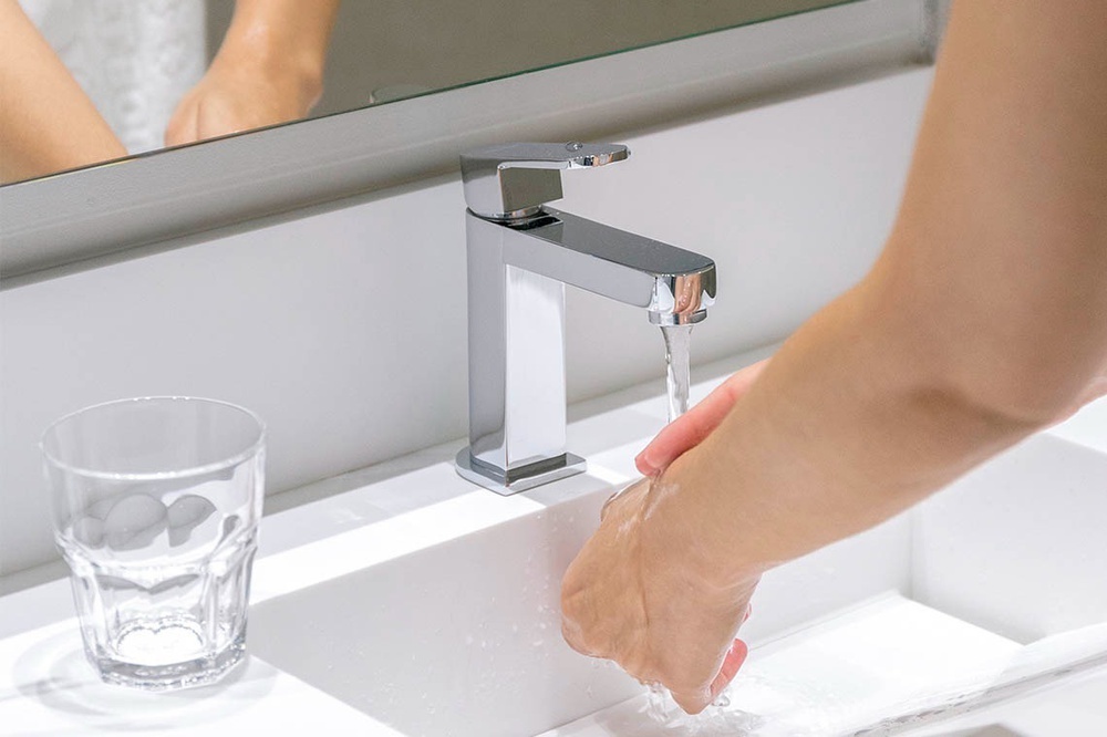 una persona se lava las manos en un lavabo junto a un vaso