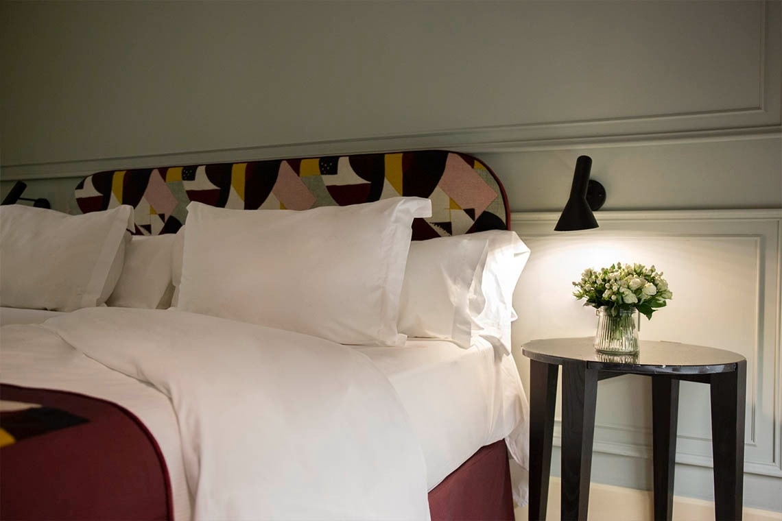 a nightstand with a vase of flowers sits next to a bed