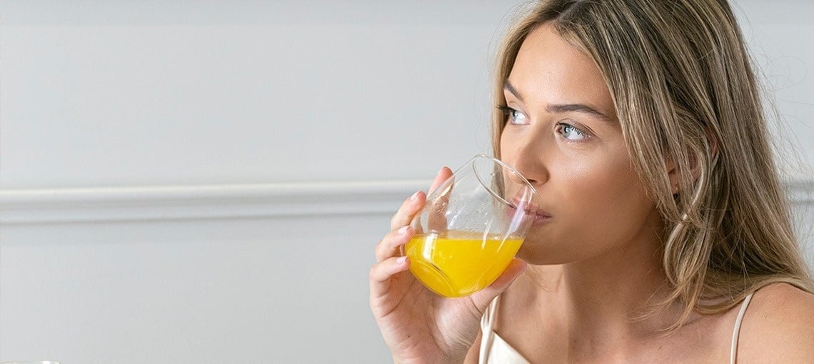 una mujer está bebiendo un vaso de jugo de naranja