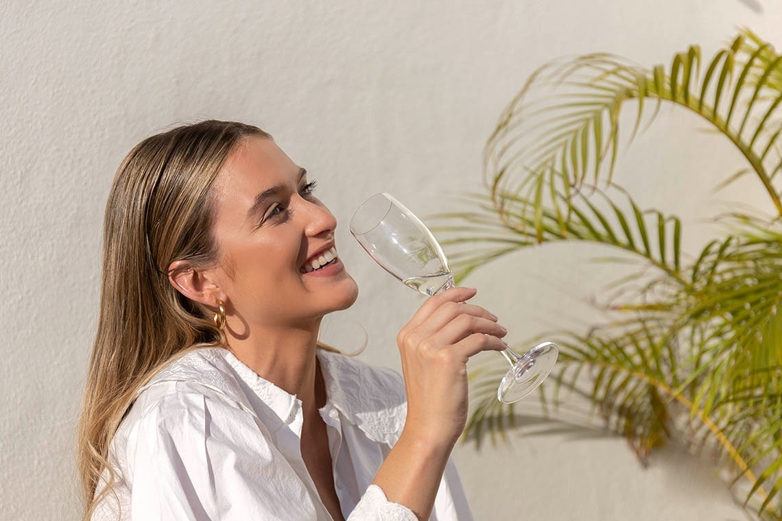 a woman in a white shirt is drinking a glass of wine