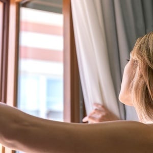 una mujer está abriendo las cortinas y mirando por la ventana