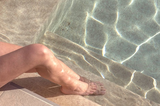 una mujer se sienta en las escaleras de una piscina con los pies en el agua